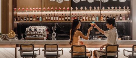 A bar area with multiple seating arrangements and a variety of bottles on shelves.