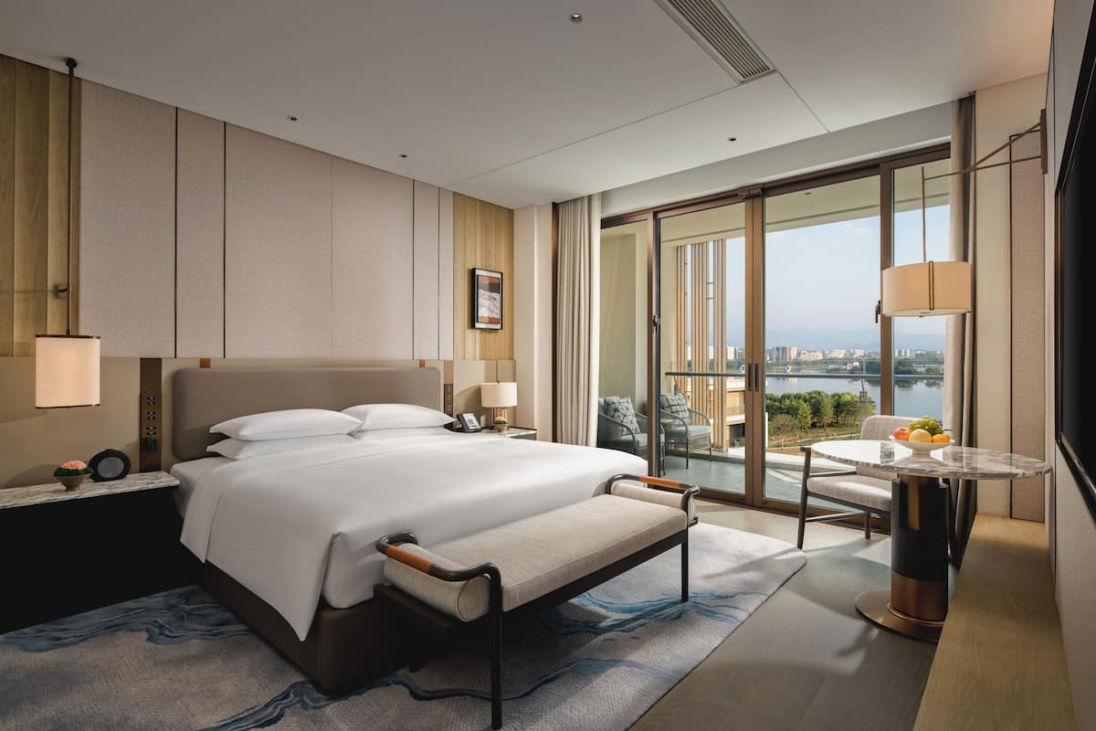 Une chambre d’hôtel moderne dotée d’un grand lit, d’un bureau avec une chaise, d’une vue sur la ville et d’un balcon avec une table et des chaises.