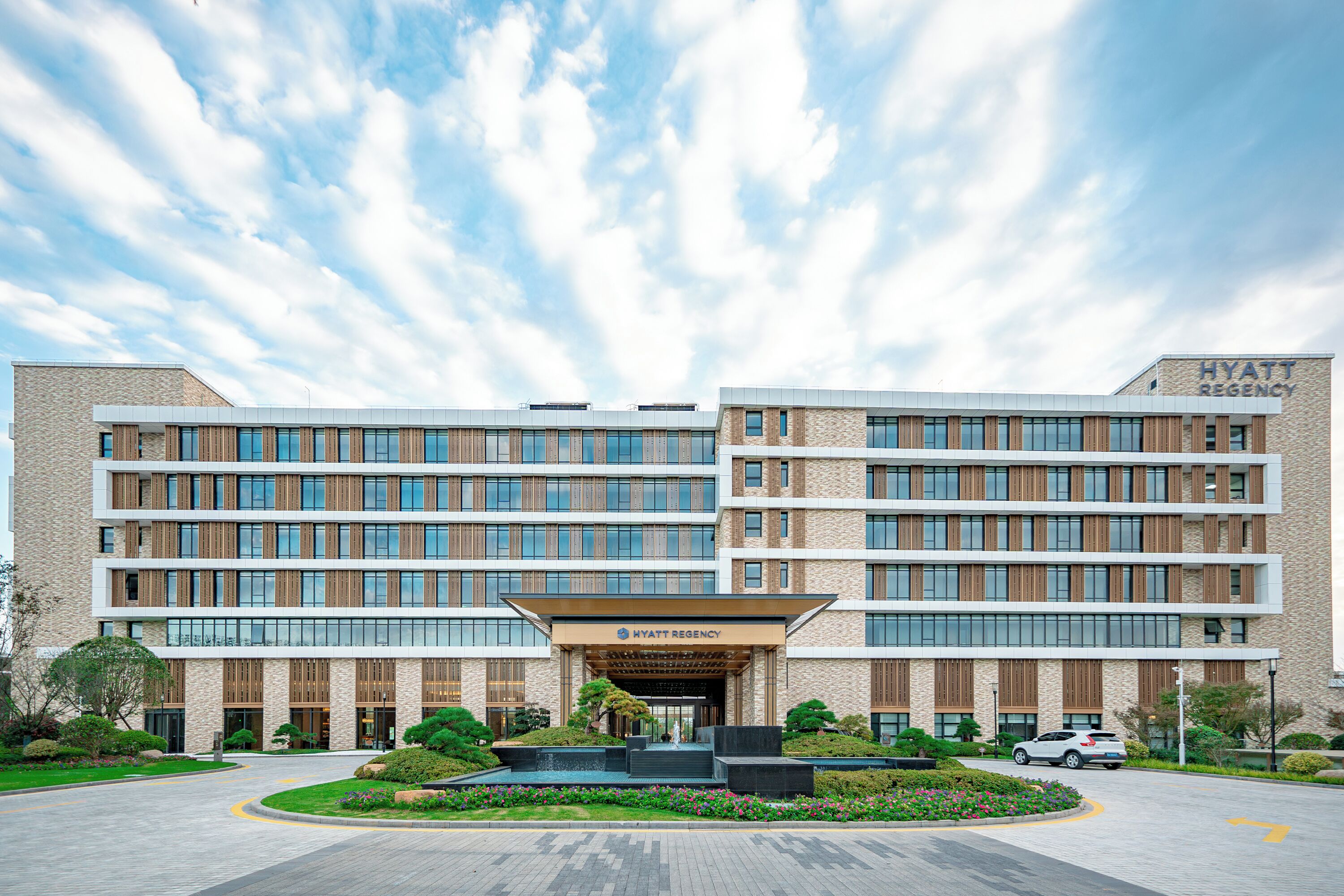A modern hotel building with a prominent entrance, multiple floors, and a landscaped area in front.