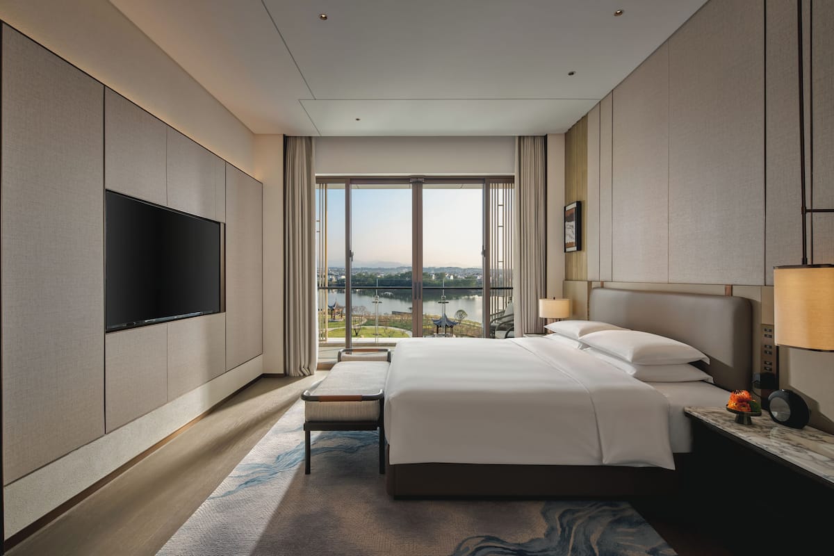 Une chambre d’hôtel moderne dotée d’un grand lit, d’une télévision à écran plat, d’une vue sur un lac et d’un balcon.