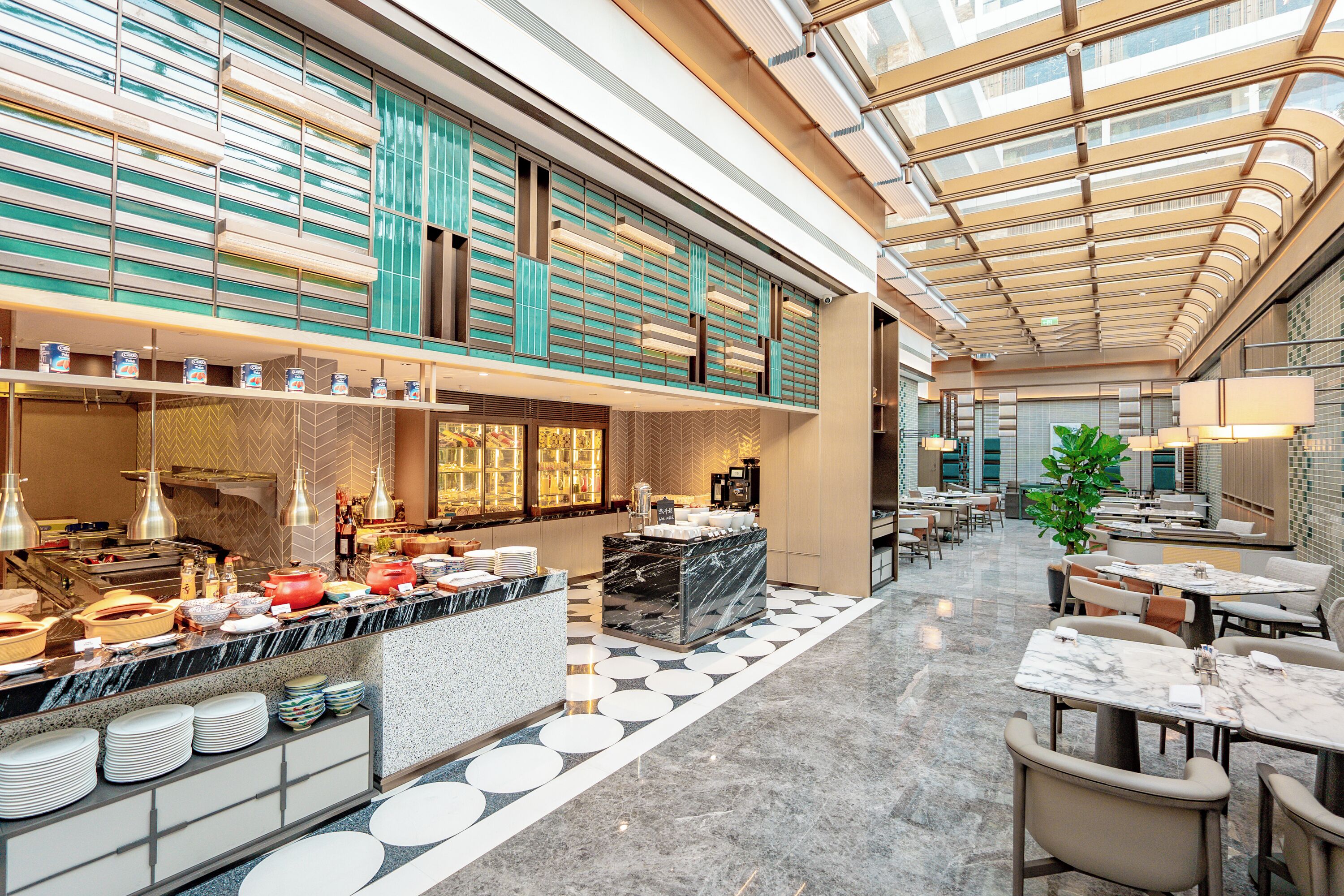 A modern hotel lobby with a central bar area, seating arrangements, and a high ceiling with skylights.