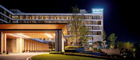A modern hotel with a prominent sign, a well-lit entrance, and a landscaped area.