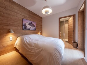 Quarto com parede de madeira, cama, quadro pendurado e porta para área de chuveiro.