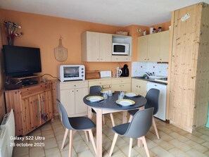 Una cocina compacta con una mesa de comedor, sillas, microondas, tostadora y televisión.