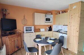 A compact kitchen with a dining table, chairs, a microwave, a toaster, and a television. - Cozy studio 200m from slopes with balcony and TV - No pets allowed (Les Adrets-Prapoutel)
