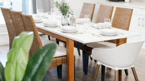 Comedor con una mesa de madera dispuesta para seis comensales, rodeada de sillas de mimbre y blancas.
