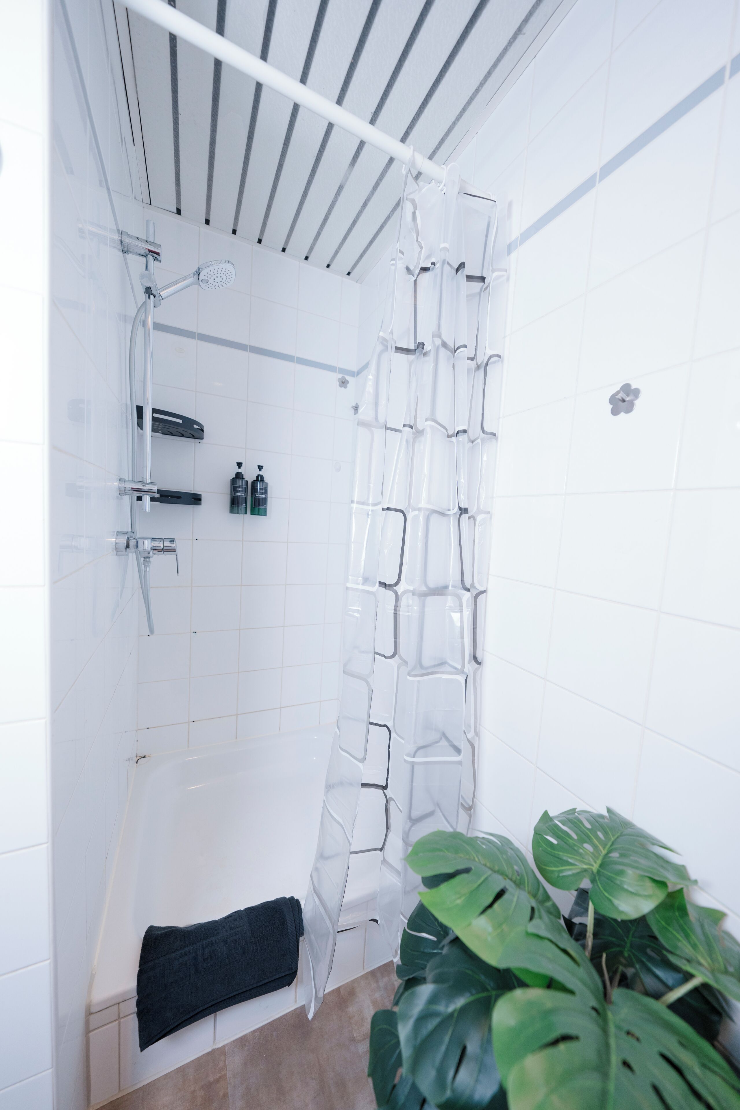 Eine Dusche mit einer transparenten Duschvorhang, einem Duschkopf zum Händhalten und einer Seifenspender für die Hand.