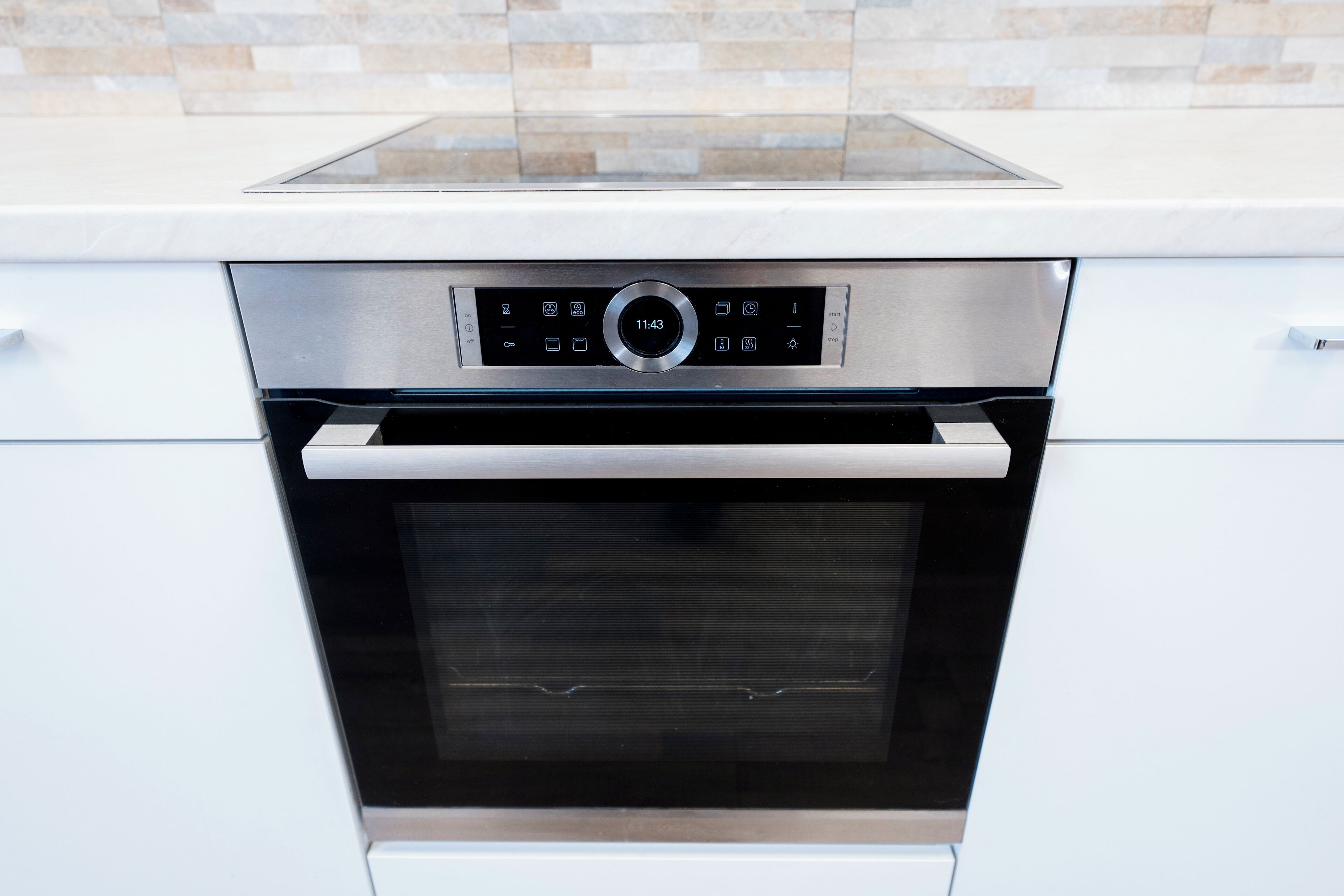 A modern kitchen with a built-in oven and a control panel displaying the time as 11:43.
