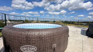 Un jacuzzi con revestimiento de mimbre, identificado como "LAY-Z-SPA ST. MORITZ", en un patio con cielo despejado y edificios al fondo.