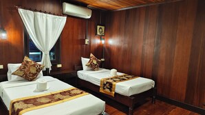A hotel room with two beds, wooden flooring, a ceiling fan, and an air conditioning unit.