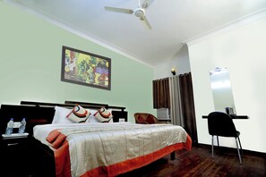 Habitación de hotel con cama, escritorio, silla, ventilador de techo y un cuadro en la pared.