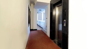 Un couloir avec un tapis rouge, un ascenseur noir et un mur blanc orné d’un motif.