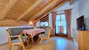 Une pièce chaleureuse avec un plafond en bois, une table à manger avec des chaises, un téléviseur posé sur un meuble en bois et une fenêtre avec des rideaux.