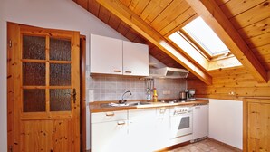 Une cuisine avec des poutres en bois, un puits de lumière, des armoires blanches et un four encastré.
