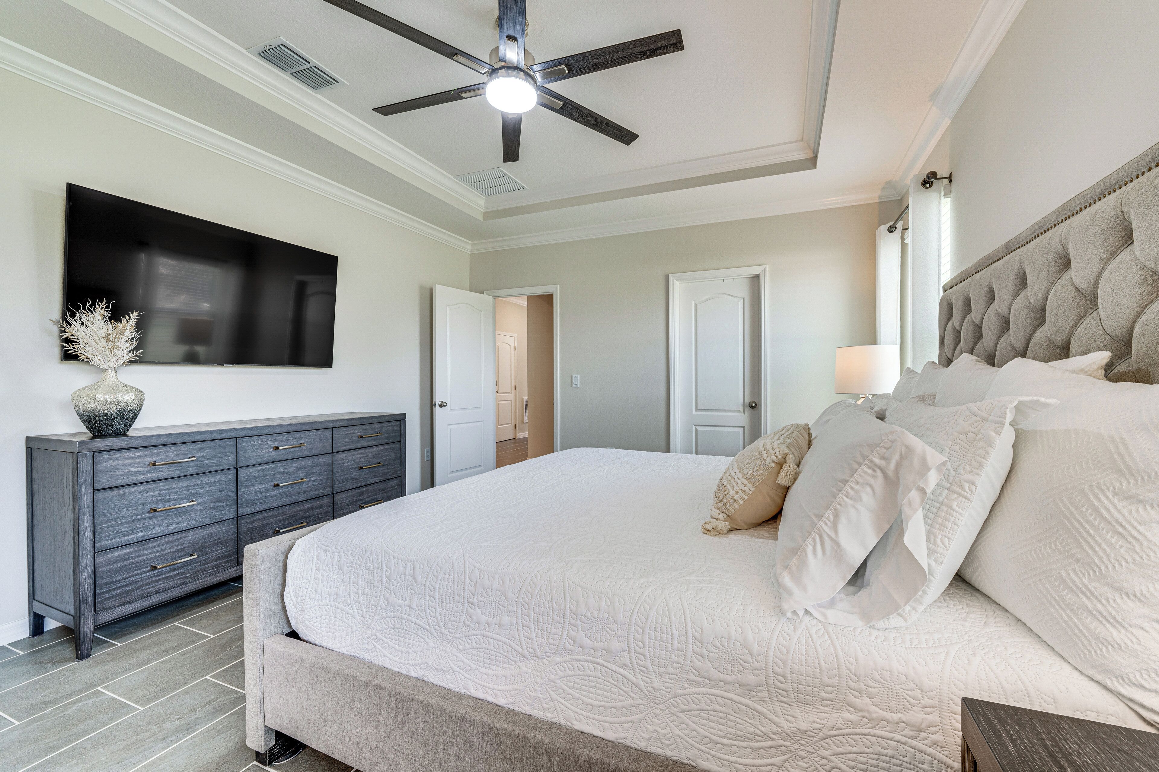 Un dormitorio con una cama grande, un aparador oscuro, un televisor de pantalla plana y un ventilador de techo.