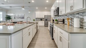 A modern kitchen with a large island, stainless steel appliances, and pendant lighting. - Relax, Play, Swim: Luxe Haines City Home w/ Lanai! (Haines City)