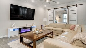 A living room with a large flat-screen TV, a wooden coffee table, a beige sofa, and a white entertainment unit with a fireplace. - Relax, Play, Swim: Luxe Haines City Home w/ Lanai! (Haines City)