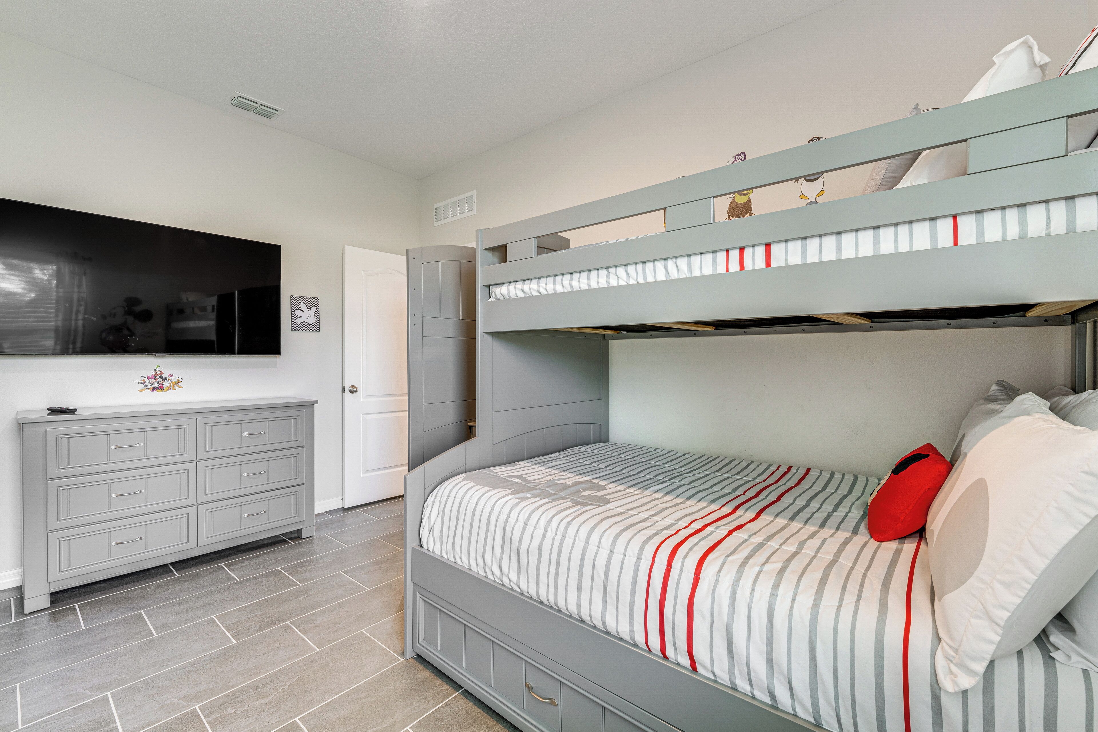 A bedroom with a bunk bed, a dresser, and a television on the wall.