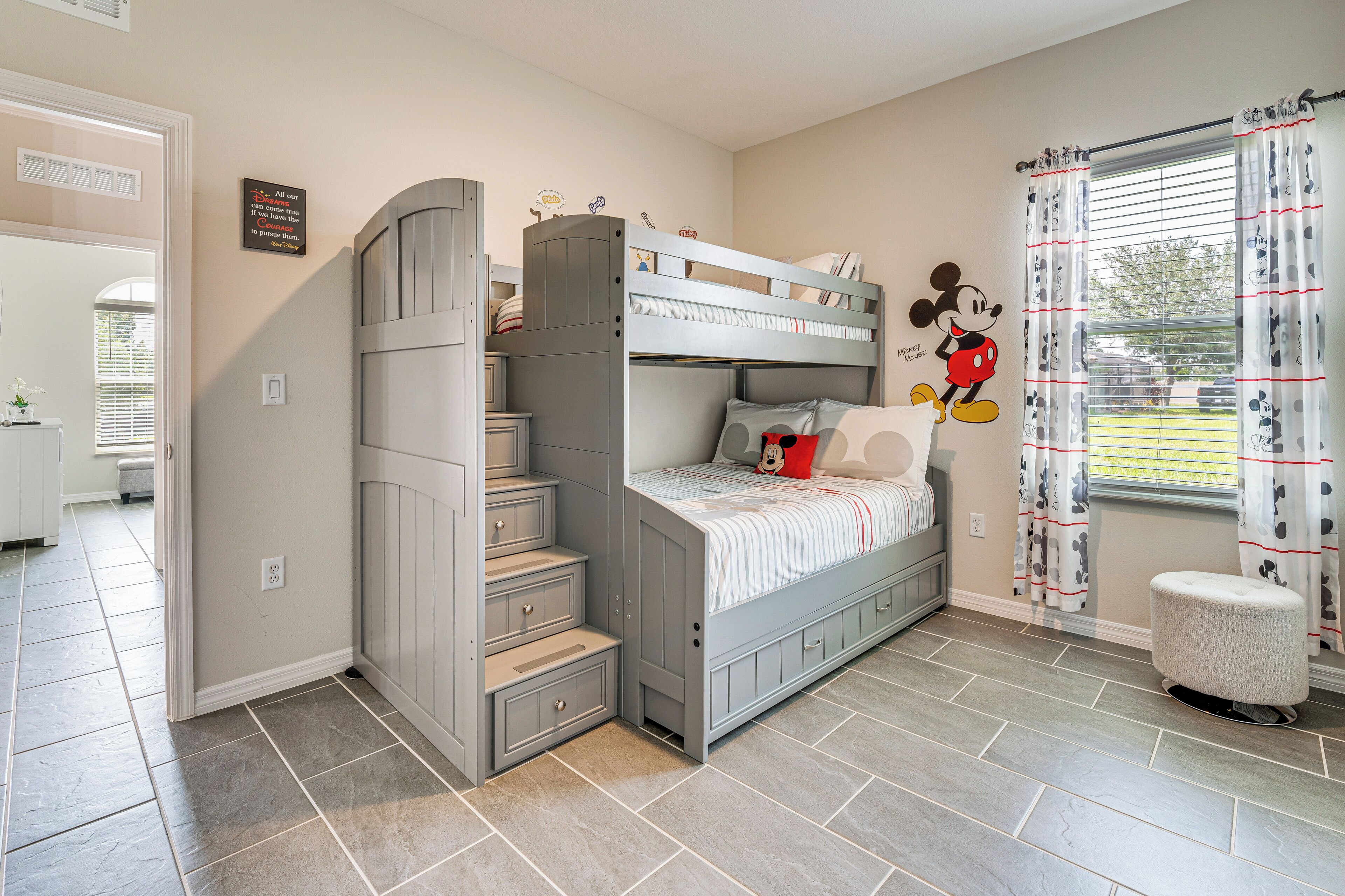 A child's bedroom with a bunk bed, a Mickey Mouse wall decal, and a window with curtains.