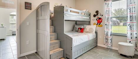 A child's bedroom with a bunk bed, a Mickey Mouse wall decal, and a window with curtains.