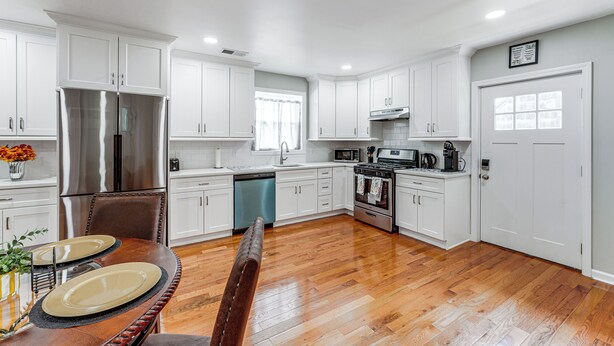 A modern kitchen with white cabinets, stainless steel appliances, and a wooden dining table. - 2 Mi to Dtwn: Well-appointed Bridgeport Duplex! (Bridgeport)