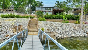 Eine Holzbrücke führt zu einem modernen Haus mit einer Steinschmalseite und üppiger Vegetation.