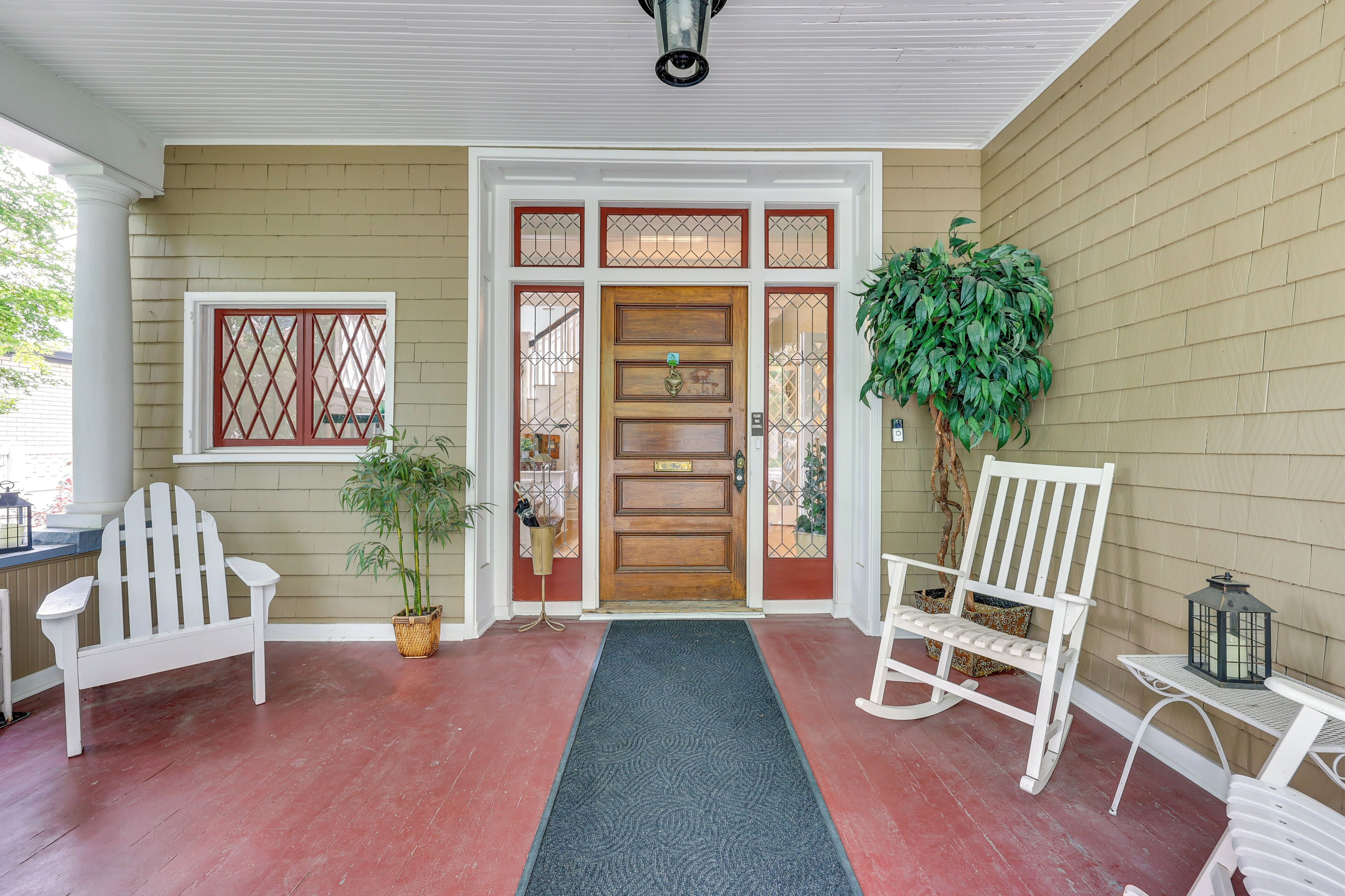 A porch with a wooden door, two Adirondack chairs, a potted plant, and a lantern on a table.
