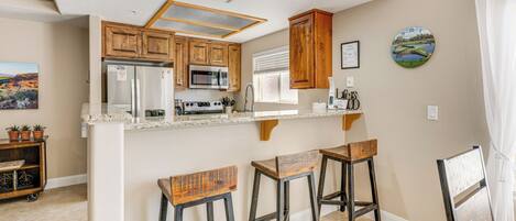 A kitchen with wooden cabinets, a microwave, a refrigerator, and a bar area with stools.