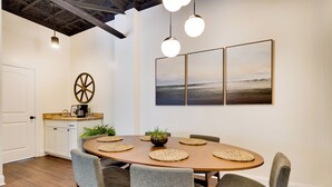 Een eetgedeelte met een ronde tafel, zes grijze bekleden stoelen en drie hanglampen.