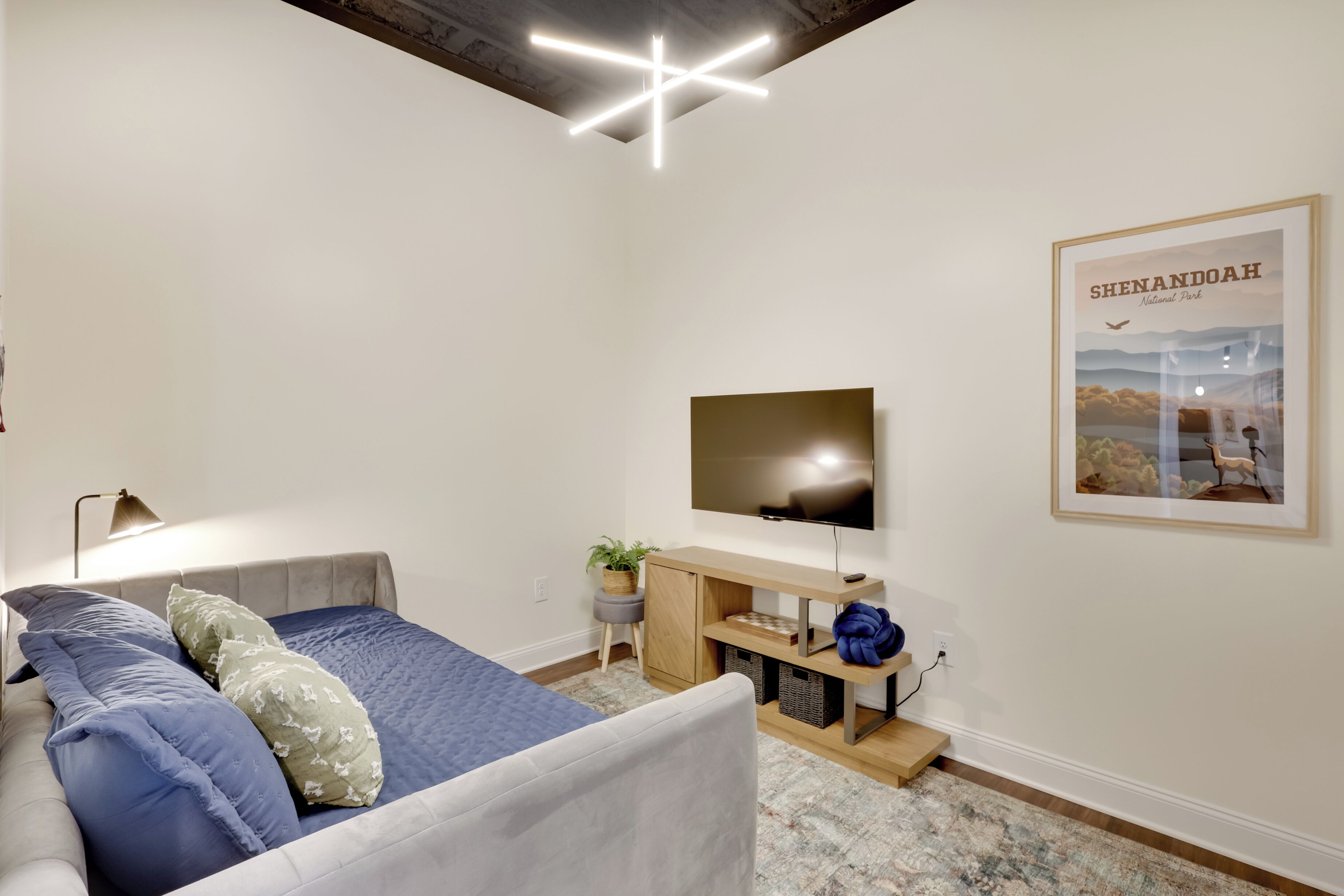 A modern bedroom with a bed, a desk, a TV, and a framed poster.