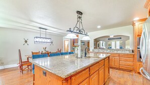 A spacious kitchen with wooden cabinets, a granite countertop island, and a hanging light fixture. - Fire Pit + Sauna: Spacious Lake Texoma Retreat! (Denison)