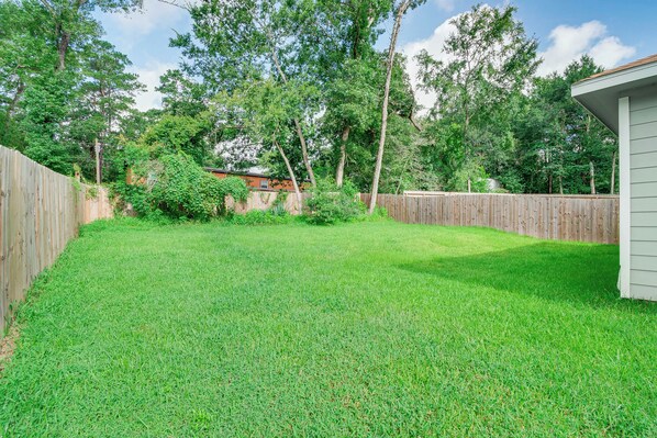 A backyard with a wooden fence, a grassy lawn, and trees in the background. - Montgomery Cottage w/ Fenced Yard < 1 Mi to Lakes! (Montgomery)