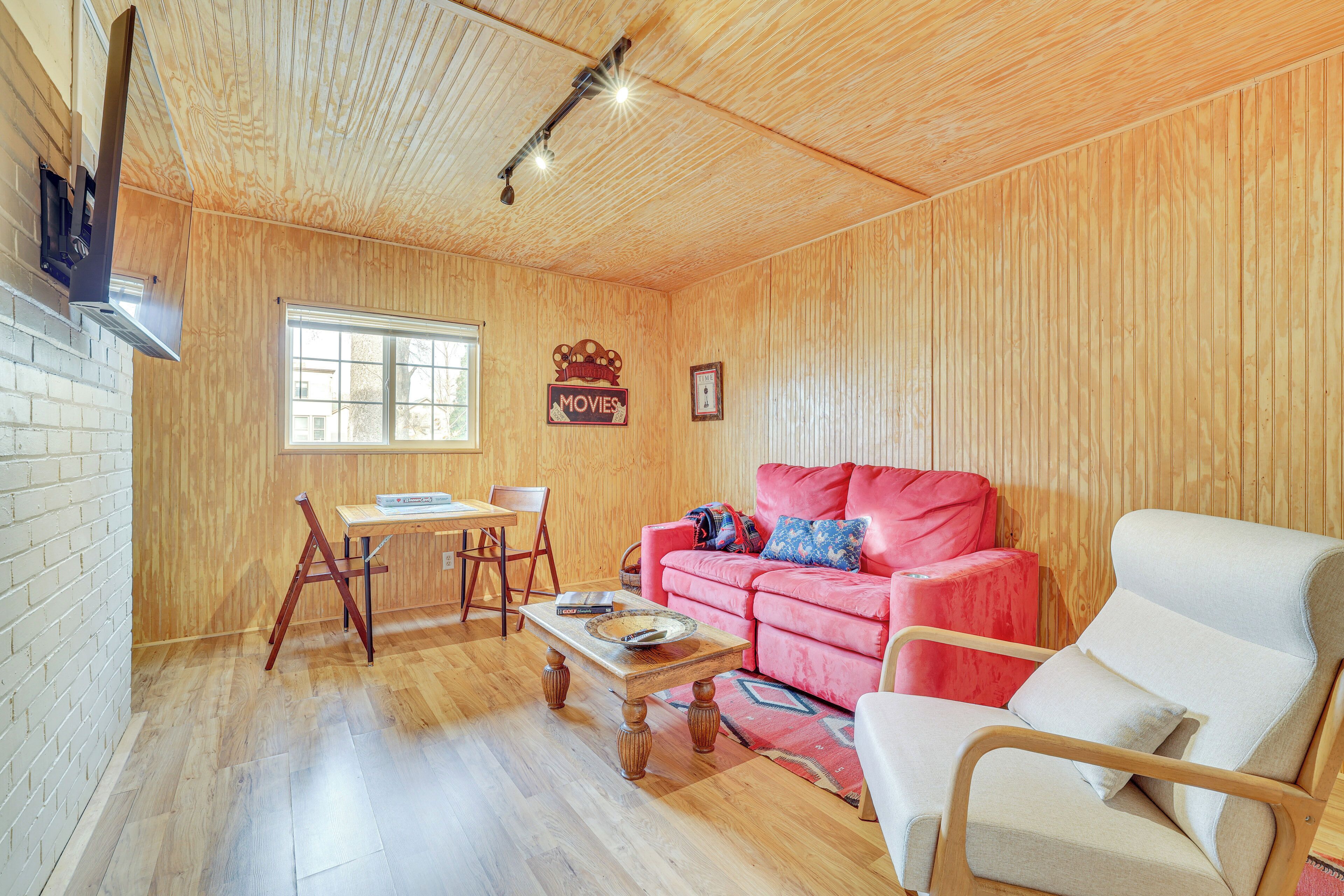 Un salon chaleureux avec un plafond en bois, un canapé rouge, un fauteuil blanc, une table basse en bois et une petite table avec des chaises.