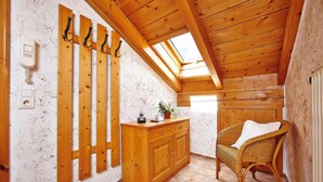 Un intérieur en bois avec un plafond en pente, une chaise en osier, un meuble en bois et un téléphone fixé au mur.