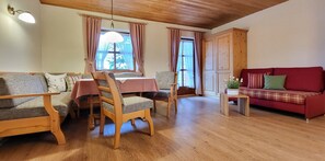 A cozy living room with wooden furniture, a red sofa, a dining table with chairs, and a wooden cabinet. - Cozy 1-room apartment with terrace and mountain view (Oberau)