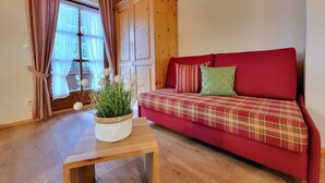 A cozy room with a red sofa, wooden cabinet, and a small table with a plant. - Cozy 1-room apartment with terrace and mountain view (Oberau)
