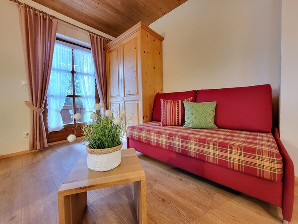 A cozy room with a red sofa, wooden cabinet, and a small table with a plant. - Cozy 1-room apartment with terrace and mountain view (Oberau)