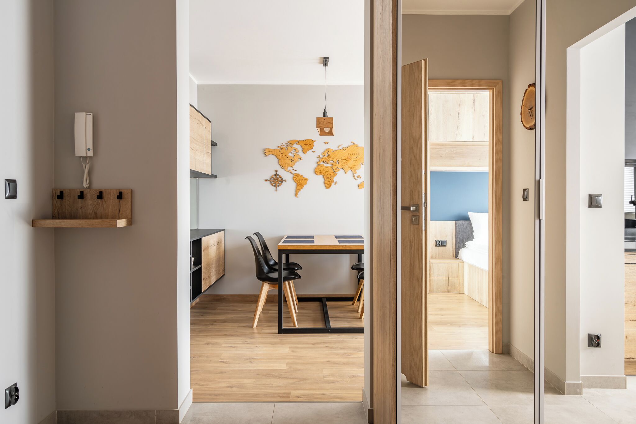 A modern kitchen with a wooden table and chairs, a world map wall decoration, and a hanging light fixture.