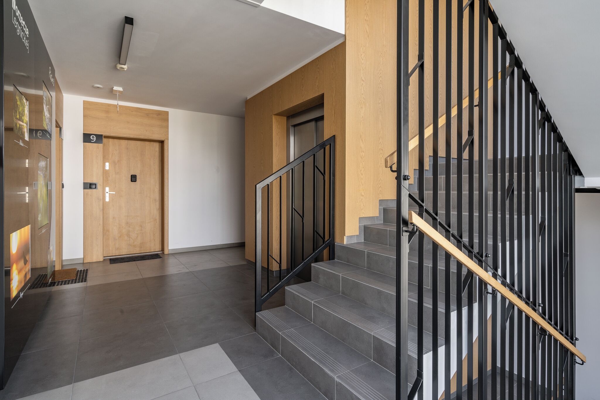 Un intérieur moderne avec un escalier, une porte en bois et un sol carrelé.