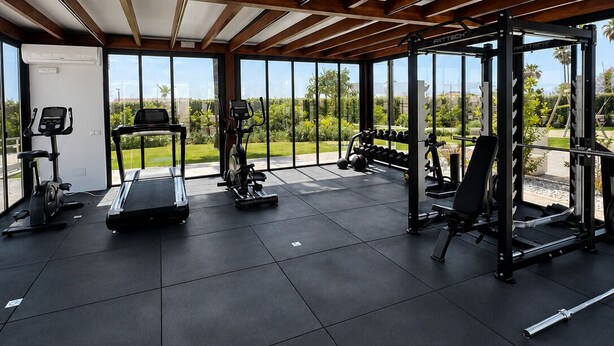 Ett gym med träningsutrustning, stora fönster och utsikt över grönområden.