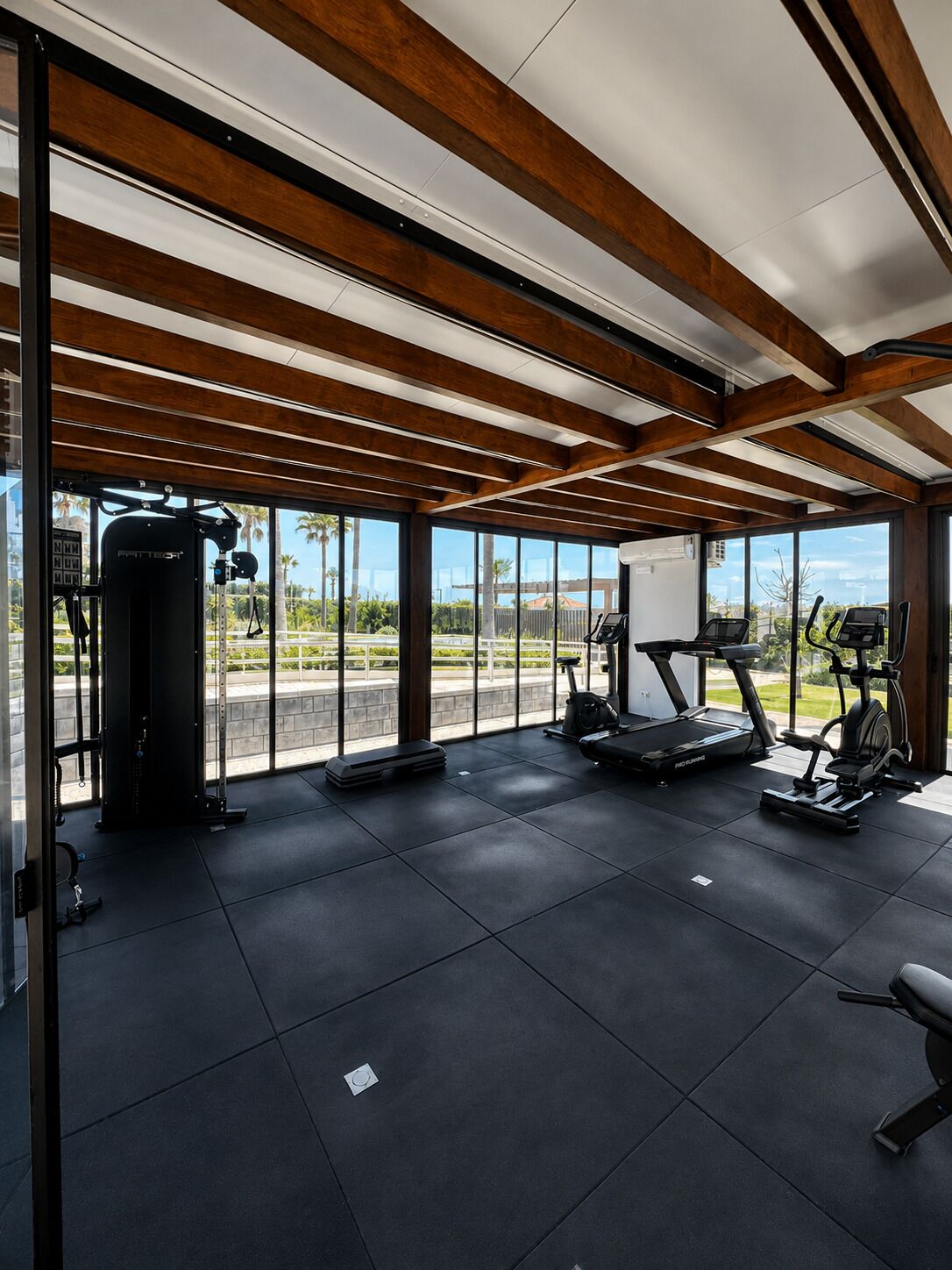 Une salle de sport équipée de matériel d’exercice, dotée de grandes fenêtres et offrant une vue sur l’extérieur.
