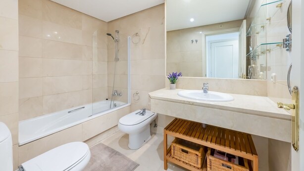 A modern bathroom with a bathtub, toilet, and sink, featuring a large mirror and a wooden shelf. - RDR409 - Best location Marina Banus with parking (Marbella)