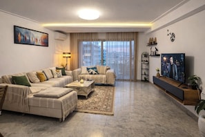 A modern living room with a sectional sofa, a coffee table, a TV, and a large window with curtains.