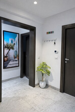 A hallway with a framed painting, a potted plant, a coat rack with keys, and a door.