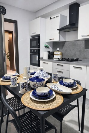 A modern kitchen with white cabinets, a black stove, and a dining table set with blue and white patterned tableware.