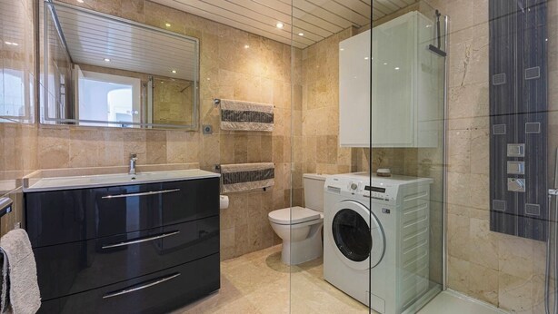 A modern bathroom with a glass shower enclosure, a black vanity with drawers, a toilet, and a front-loading washing machine. - RDR406 - Superb Costalita in Beachfront complex (Estepona)