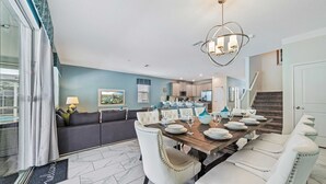 Un coin repas avec une table en bois dressée pour six personnes, des chaises à revêtement blanc et un lustre moderne.