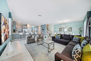 A modern living room with a sofa, coffee table, and a dining area with chairs. - Disney near Resort 9BR Home Oasis w/ Pool (Kissimmee)