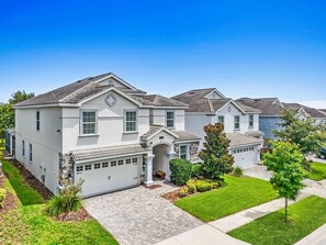 A two-story residential house with a garage, a front porch, and a well-maintained lawn. - Disney near Resort 9BR Home Oasis w/ Pool (Kissimmee)