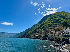 A coastal town with buildings along a waterfront, a dock, and a mountainous backdrop. - Lakeview Paradise in Argegno (Argegno)